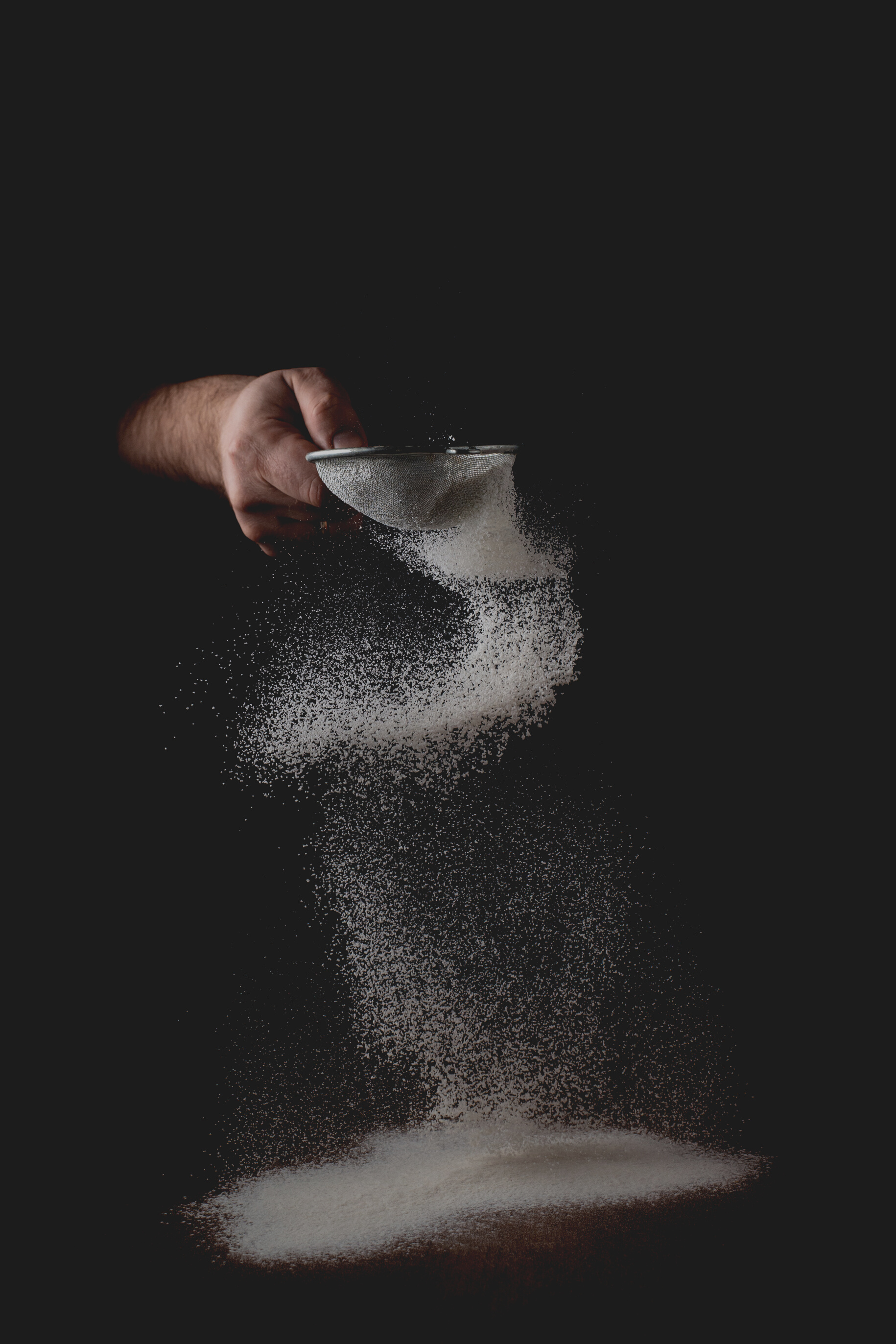 Flour Flies through a Sieve on a Black Background. a Man Sifts Flour for Cooking. Culinary Theme.